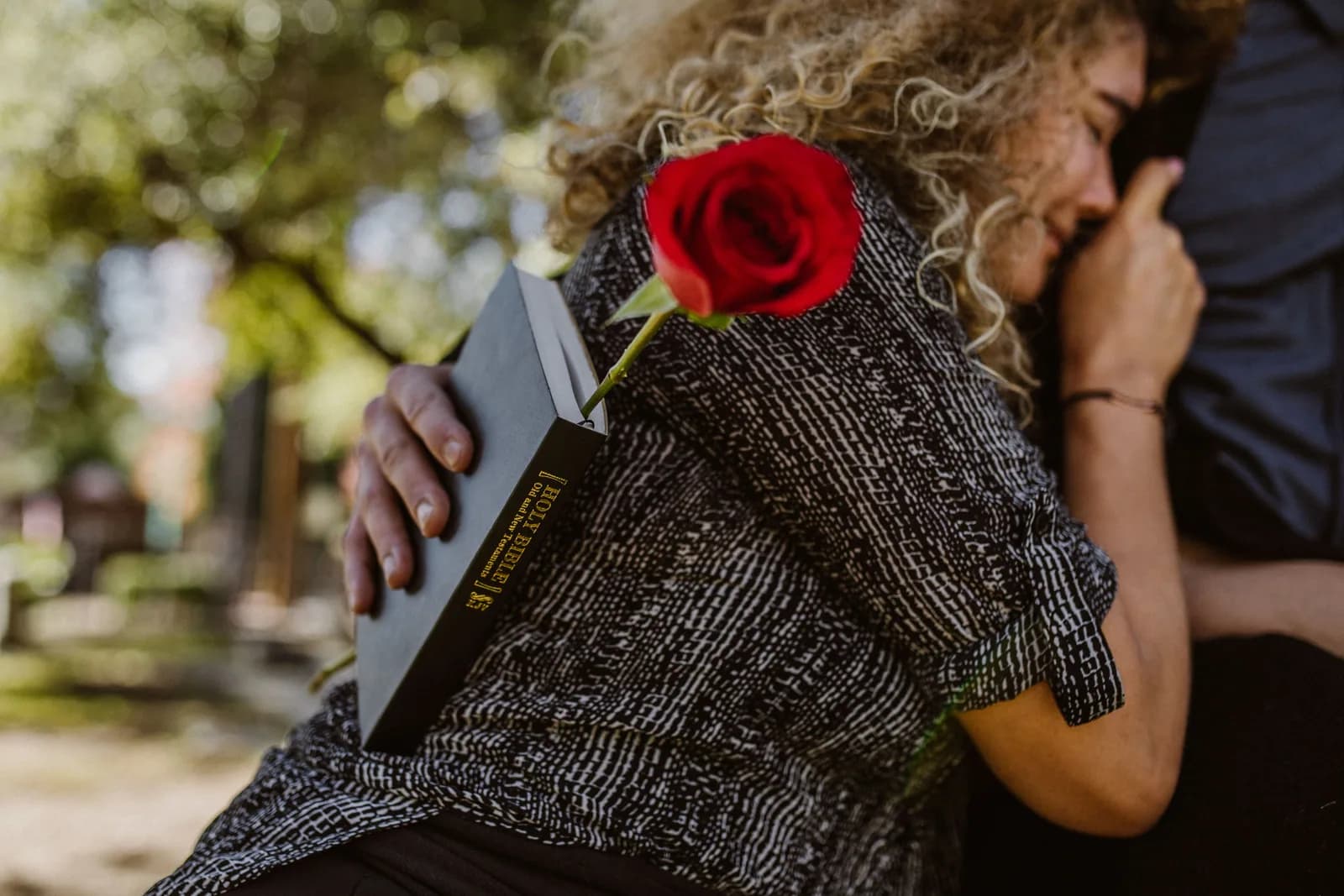 A woman holding a Bible and red rose while receiving a comforting embrace, representing compassionate biblical love
