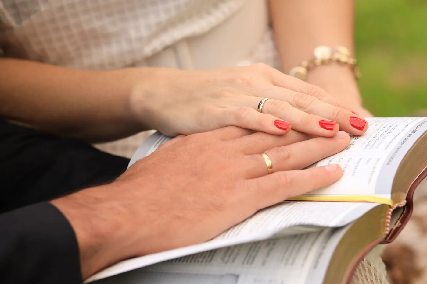 Married couple wearing wedding rings rests their hands on an open Bible